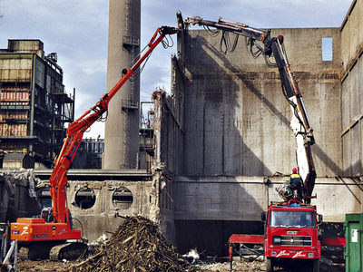 Foto di un escavatore e di un camion gru impegnati in una demolizione